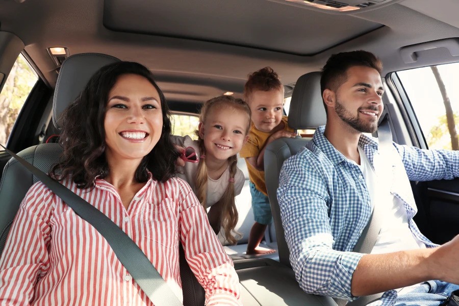 A happy family of four traveling in a car, with the parents in the front seats and two children smiling in the backseat.